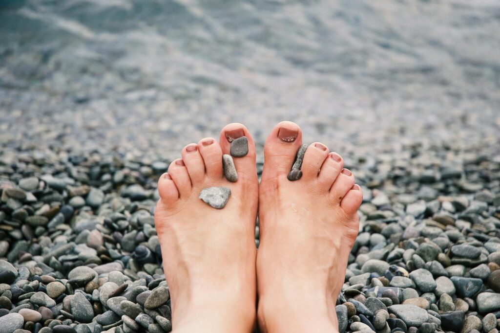 Close-up of female feet with stones on pebbled beach by the water, evoking relaxation and tranquility.